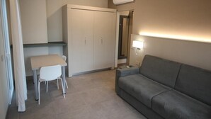 A compact room with a grey sofa, a small table with two chairs, a wardrobe, and a wall-mounted lamp. - Persea Mare 5B tutti i comfort a 2 passi dal mare (Arma di Taggia)
