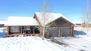 Une cabane en bois avec un porche couvert, un garage et un paysage enneigé.
