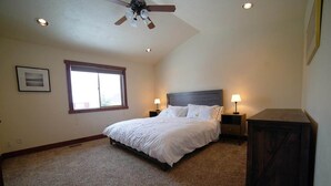 Une chambre à coucher comprenant un lit, deux tables de chevet, un ventilateur de plafond, une fenêtre et une commode en bois foncé.