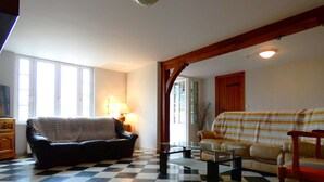 A living room with a checkered floor, a black leather sofa, a striped sofa, and a wooden chair.