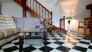 A living room with a checkered floor, a wooden staircase, a sofa, a coffee table, and two chairs.