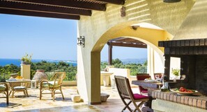 An outdoor patio with a stone fireplace, wicker furniture, and a view of the sea.
