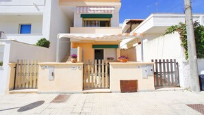 A modern two-story building with a gated entrance, a covered porch, and a small balcony with potted plants.