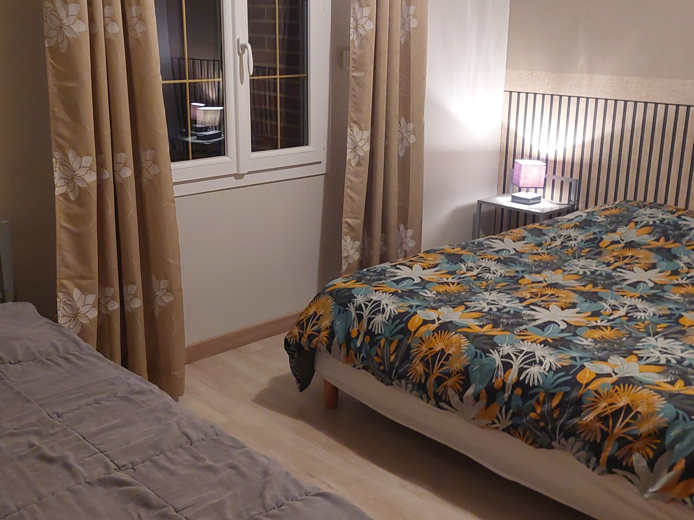 Ein Schlafzimmer mit Bett, Nachttisch, Vorhängen und einem Fenster.