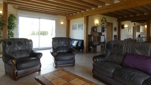 A spacious living room with leather sofas, a wooden ceiling, and a tiled floor.