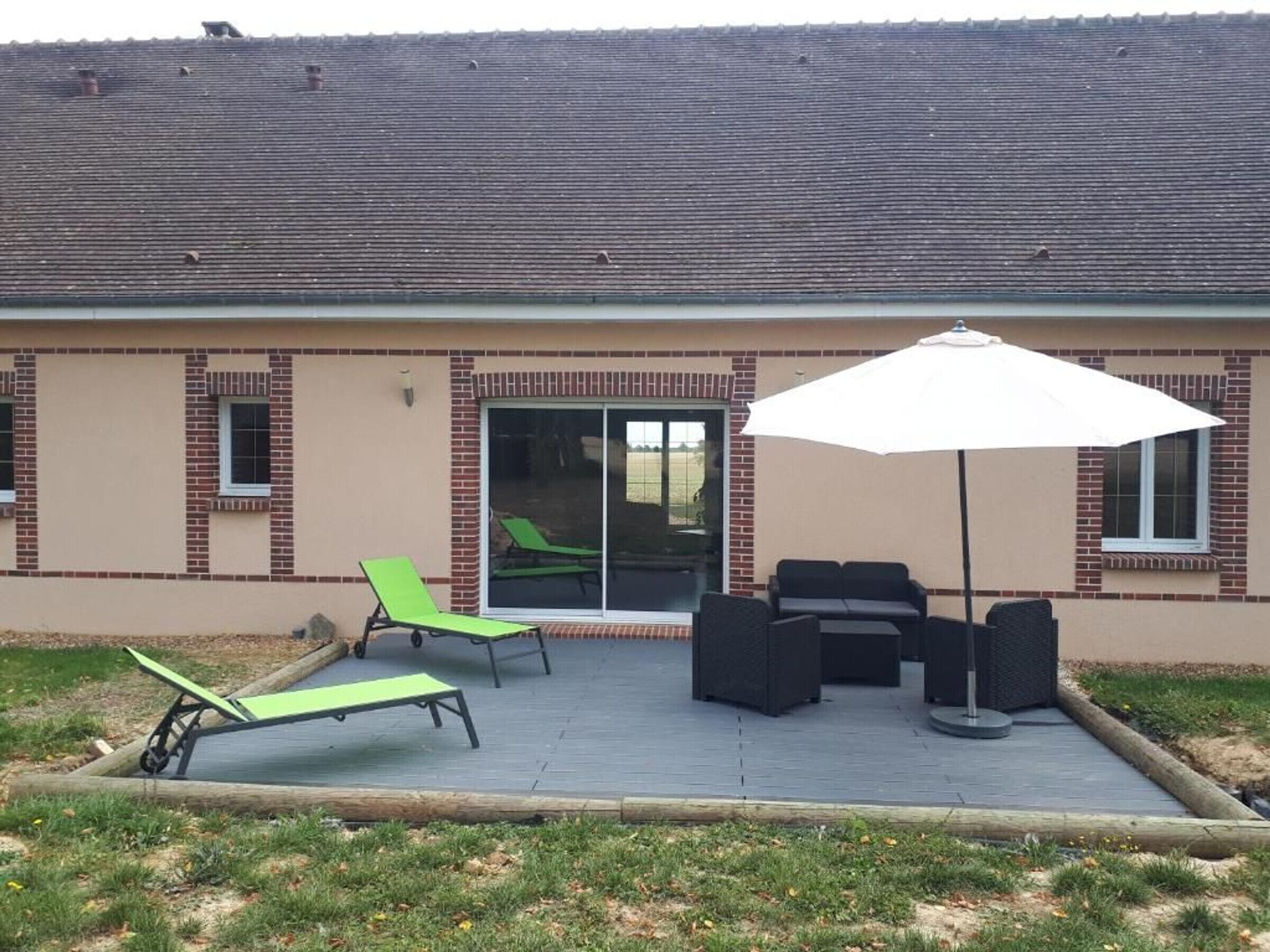 A building with a patio area featuring outdoor furniture, including two green lounge chairs and a black sofa set.