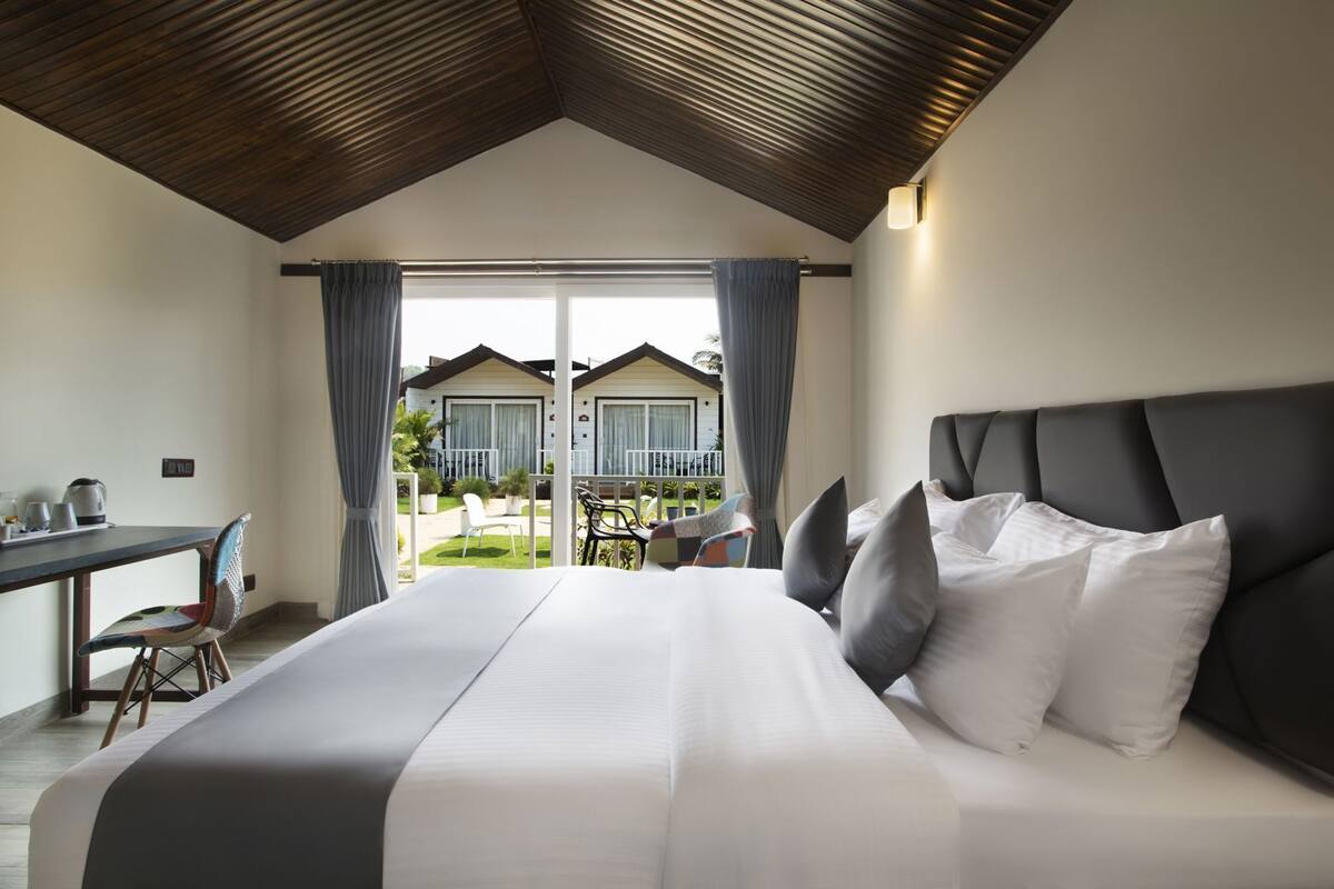 Quarto com cama grande, escrivaninha e vista para uma casa através de uma porta de correr.