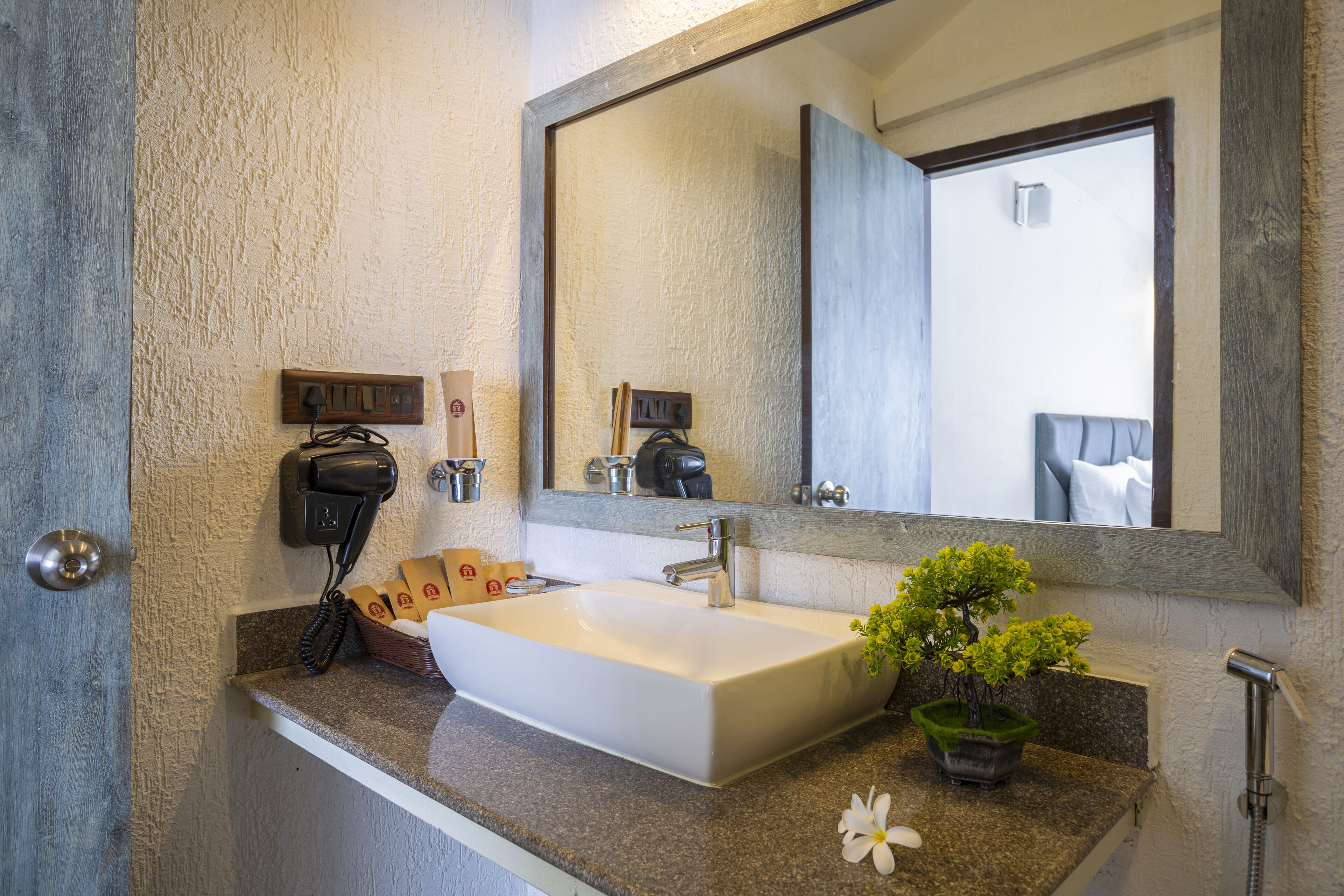 A bathroom with a white sink, a large mirror, a hairdryer, and a small potted plant.