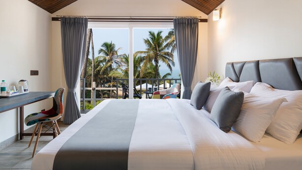 Een slaapkamer met een groot bed, een bureau en uitzicht op palmbomen en de oceaan.