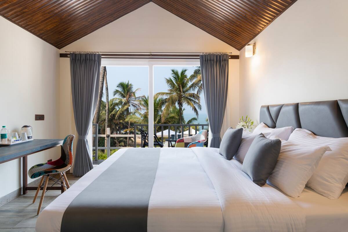 Quarto com cama grande, escrivaninha e vista para palmeiras e o oceano.