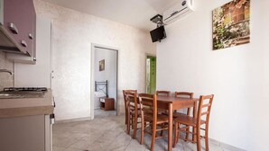 Une cuisine compacte avec un coin repas, un téléviseur fixé au mur et une porte donnant sur une autre pièce.