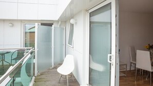 A balcony with a glass railing, a white chair, and a dining table with chairs. - Skyvillion Apartments - TowerPoint Enfield - 1Bed Deluxe Apartment w/ Balcony (Greater London)