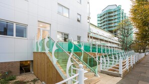 A modern building with a white exterior, a wooden fence, and a green staircase with white railings. - Skyvillion Apartments - TowerPoint Enfield - 1Bed Deluxe Apartment w/ Balcony (Greater London)