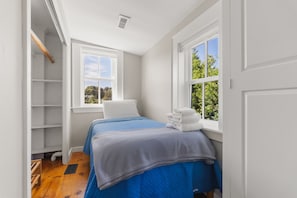 A small, bright room with a bed, a window, and a white wardrobe.