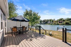 A deck with a table and chairs, overlooking a lake with boats.