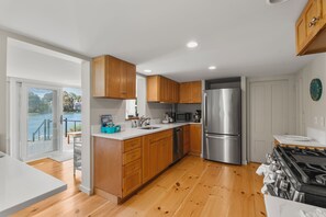 A modern kitchen with wooden cabinets, stainless steel appliances, and a view of a lake through a sliding glass door.