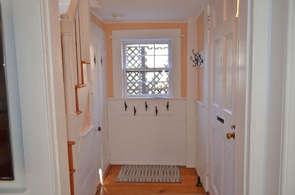 A narrow hallway with white doors, a window with a lattice design, and a patterned doormat.