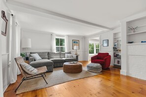 A spacious living room with a grey sectional sofa, a red armchair, a woven chair, and a wooden coffee table.