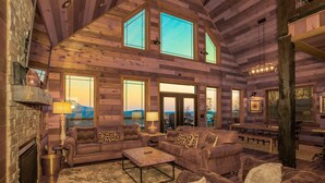A log cabin interior with a fireplace, multiple couches, a coffee table, and large windows offering views of the outdoors. - Rockin' Ridge Retreat: Indoor Pool, Mtn Views, Home Theater, Games, Signature, near Attractions! (Sevierville)