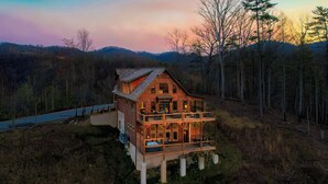 A large wooden cabin with a balcony, situated on a hill surrounded by trees. - Rockin' Ridge Retreat: Indoor Pool, Mtn Views, Home Theater, Games, Signature, near Attractions! (Sevierville)