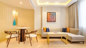 Una sala de estar moderna con una mesa redonda para comer, dos sillas de madera, un sofá con cojines de colores y un cuadro en la pared.