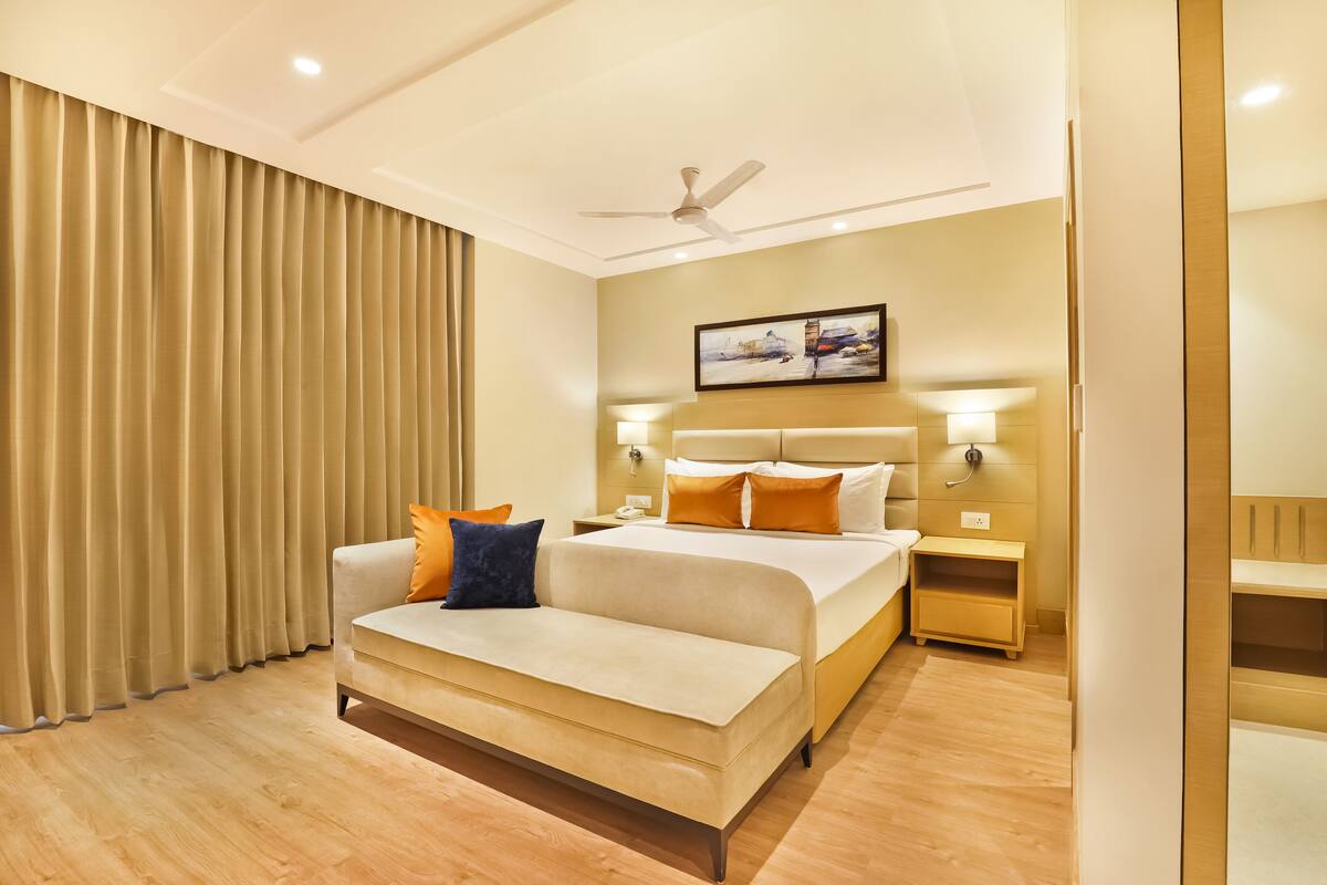 A hotel room with a bed, a sofa, a nightstand, and a ceiling fan.