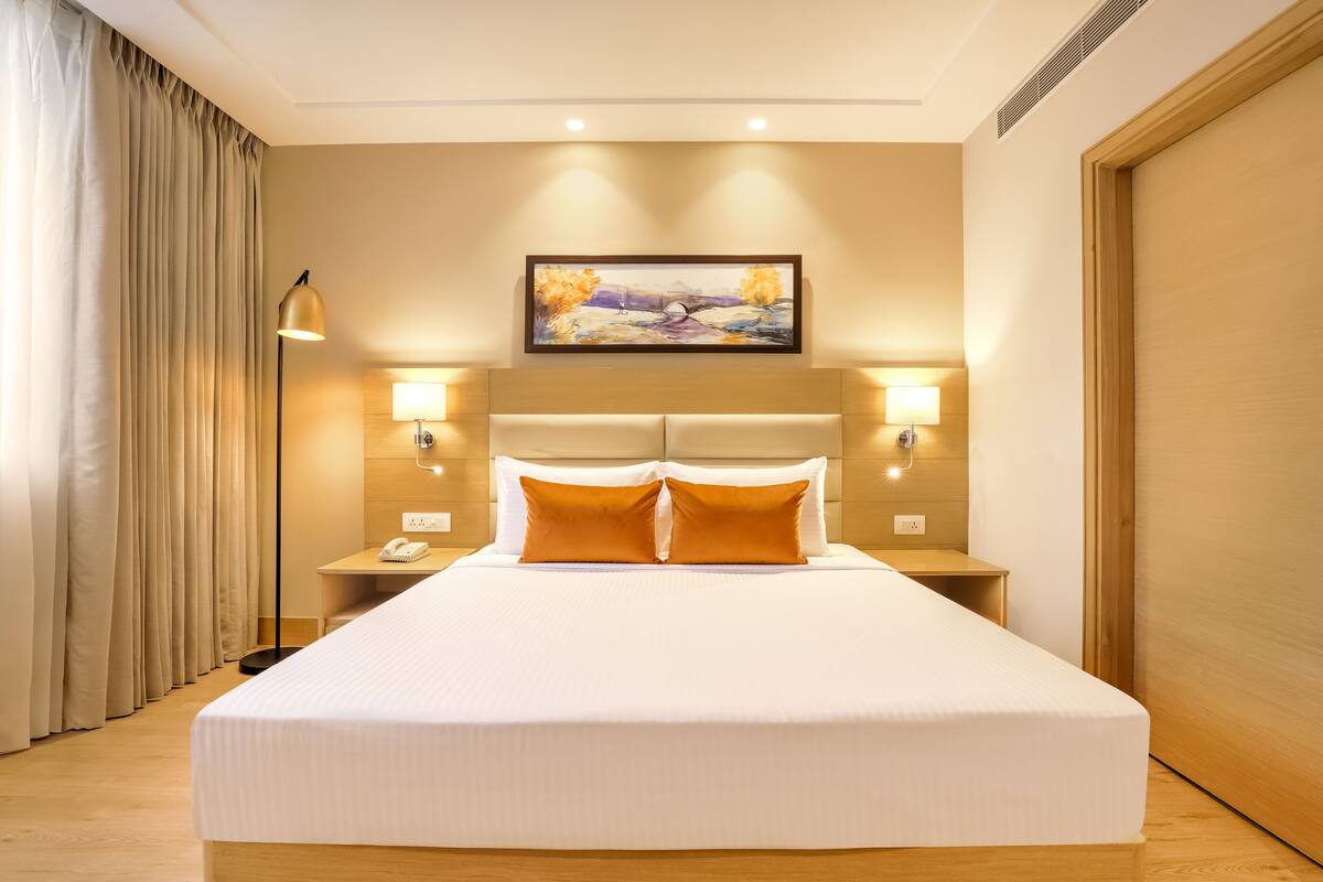 A hotel room with a large bed, two bedside tables with lamps, a painting above the bed, and a curtain on the left.