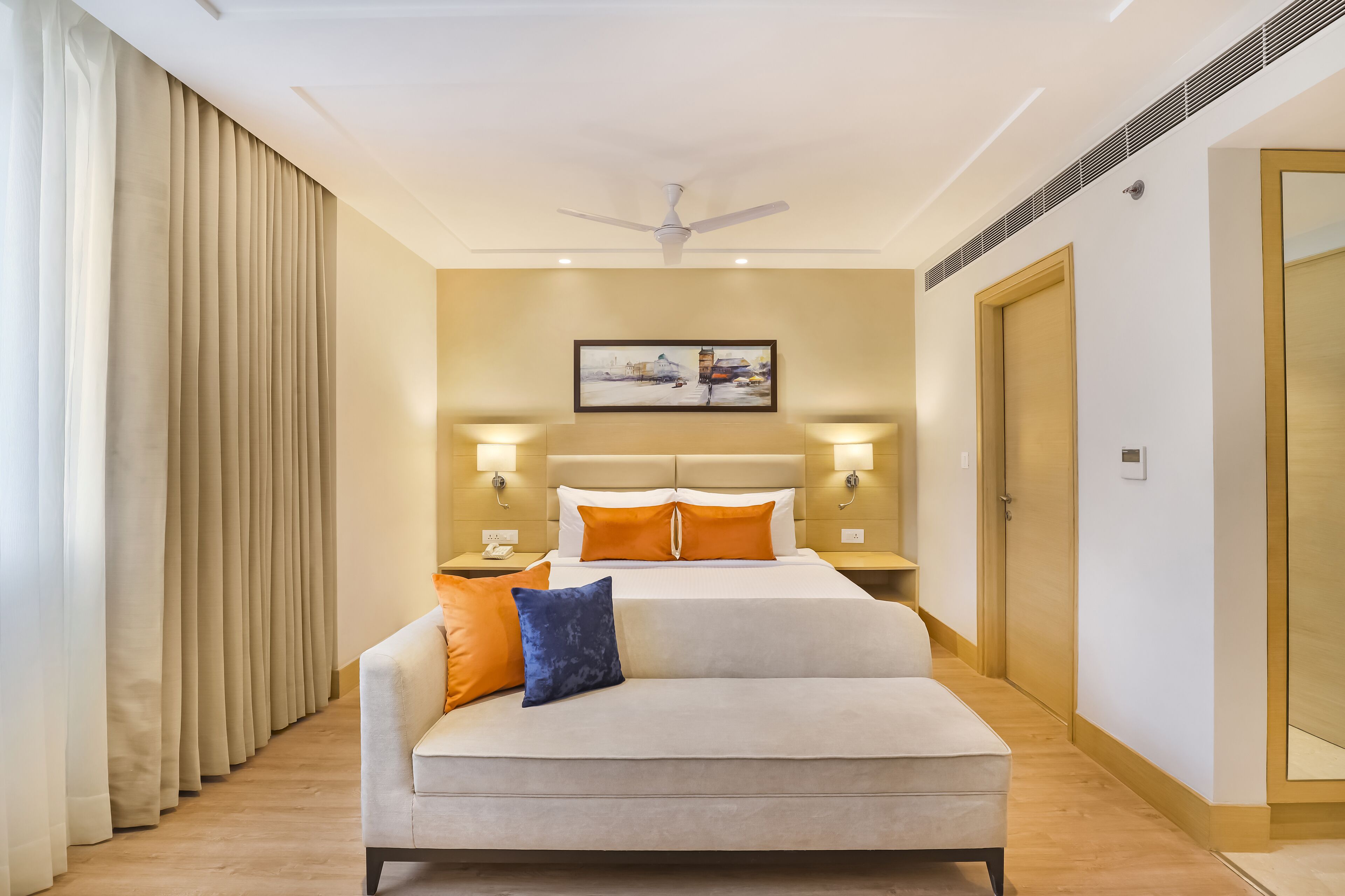 A hotel room with a bed, a sofa, a ceiling fan, and a painting on the wall.