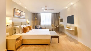 Habitación de hotel con una cama grande, mesitas de noche, un escritorio, una silla, un televisor y un ventilador de techo.