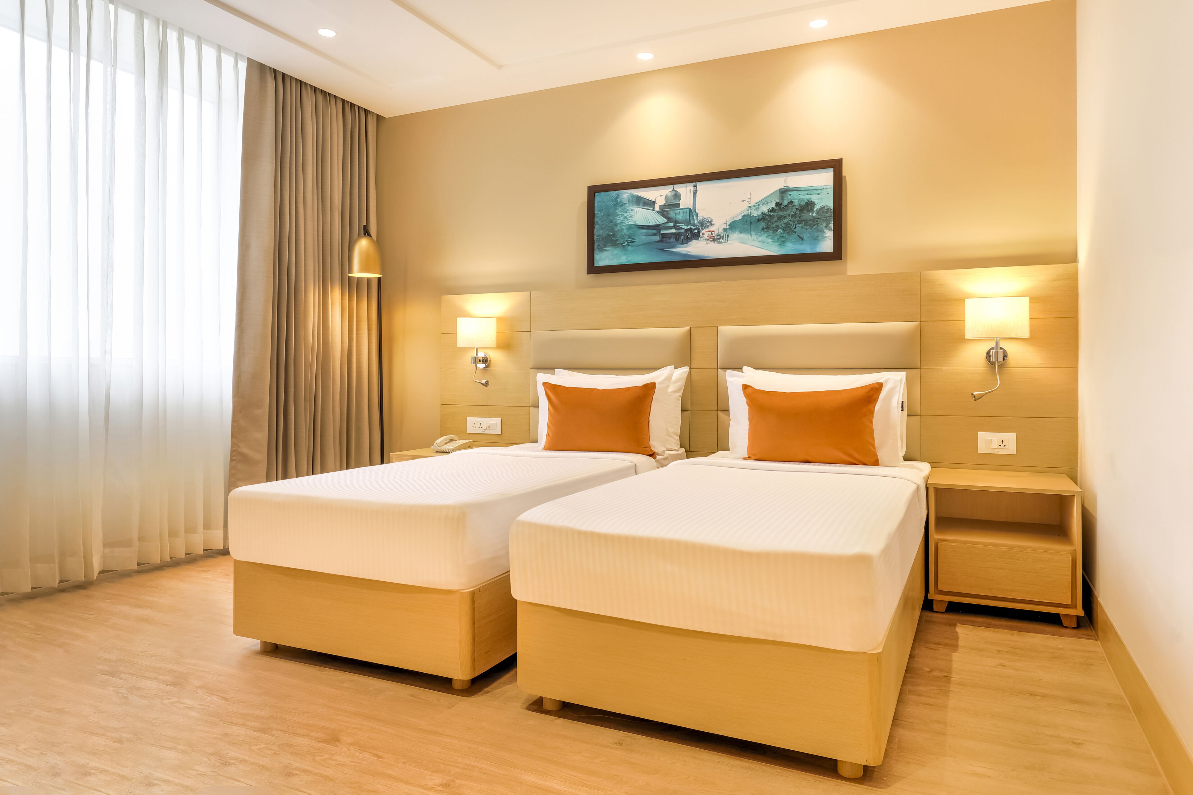 Habitación de hotel con dos camas, un ventanal con cortinas translúcidas, un cuadro en la pared y lámparas de noche.