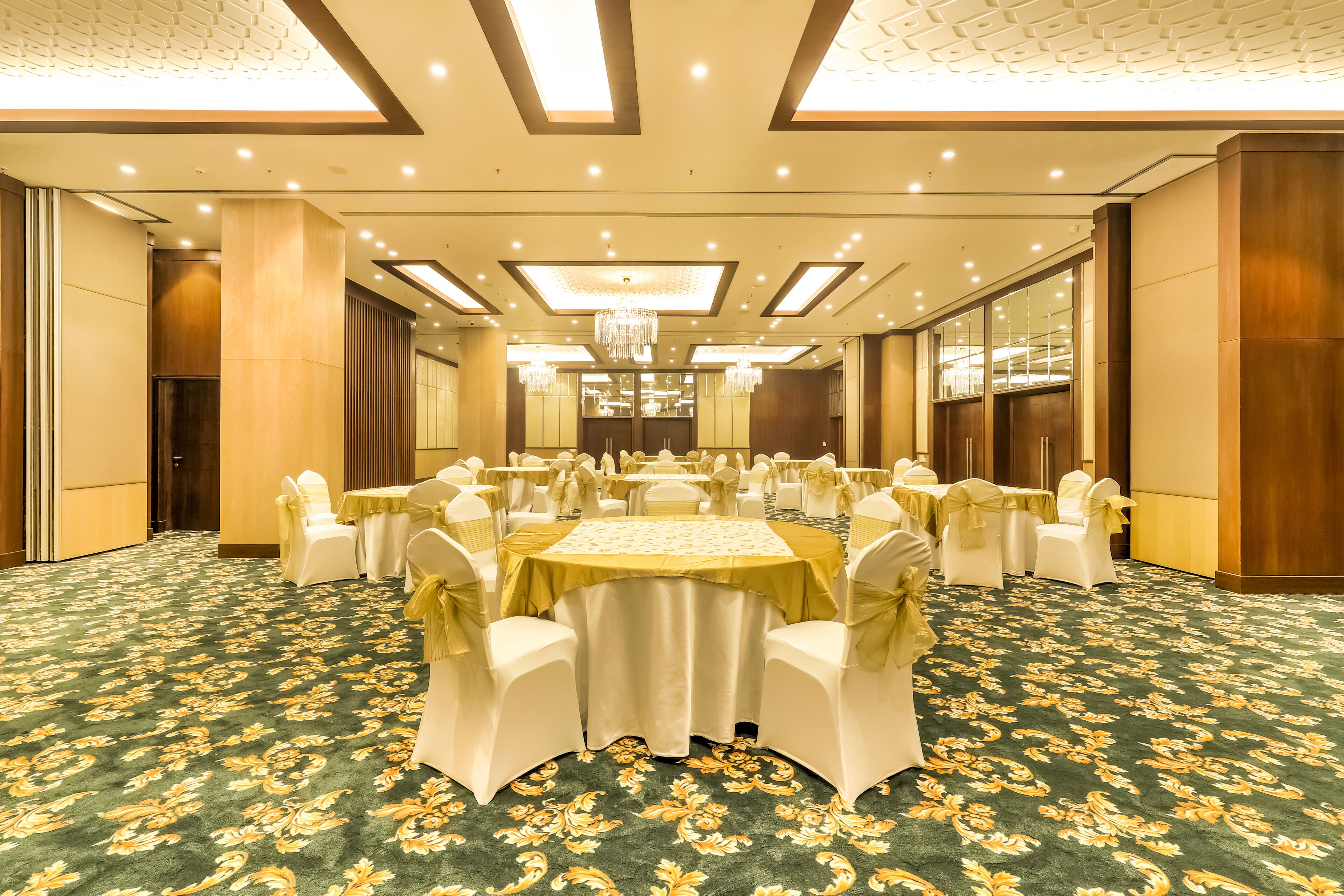 A banquet hall with round tables, white chairs, and a green carpet with a floral pattern.