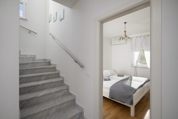 A bedroom with a bed, a window with curtains, a chandelier, and a staircase with handrails.