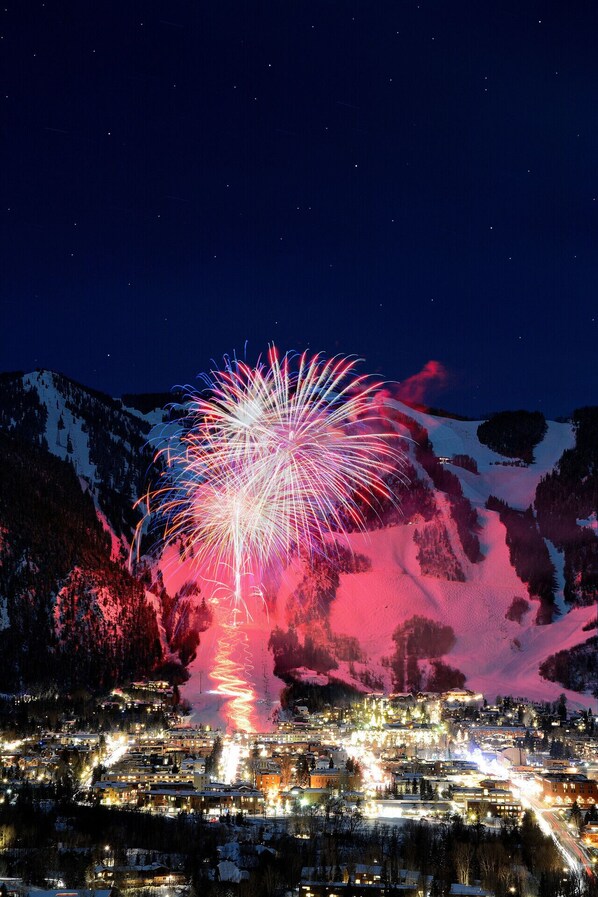 Ein belebtes Stadtbild bei Nacht mit einem farbenprächtigen Feuerwerk über einer Bergkulisse.