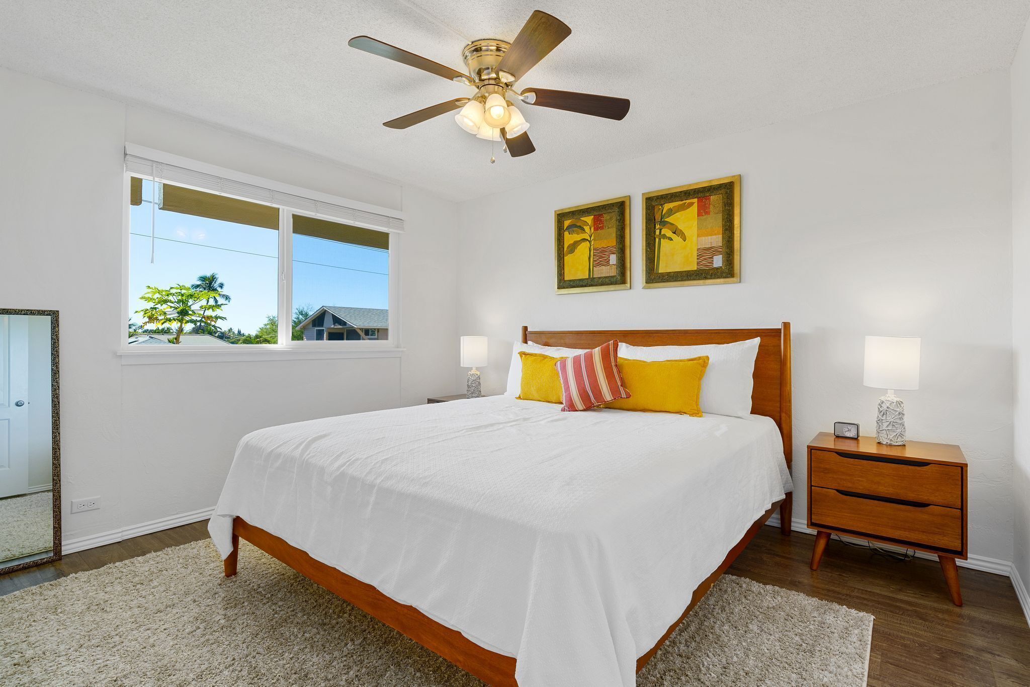 A bedroom with a bed, a nightstand, a ceiling fan, and two wall-mounted paintings.