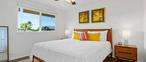 A bedroom with a bed, a nightstand, a ceiling fan, and two wall-mounted paintings.