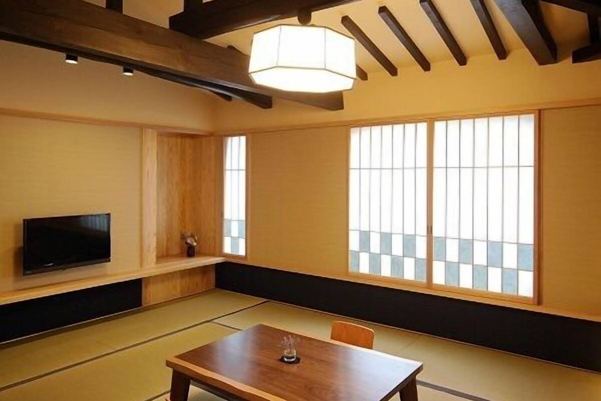 A traditional Japanese room with tatami flooring, a low table, a television, and sliding shoji doors.