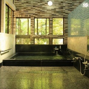 A spa room with a large rectangular hot tub, a window with a view of trees, and a tiled wall. - Motoyu Yamadaya Ryokan (Hitachiota)