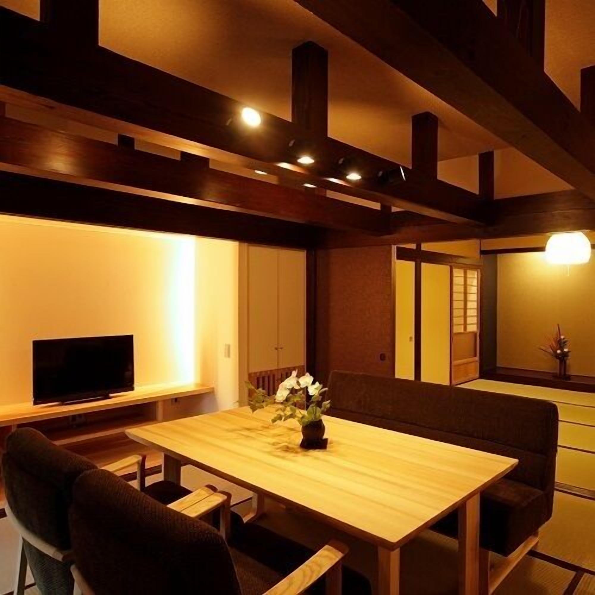 A traditional Japanese-style room with tatami flooring, a low table with cushions, and a television on a stand.
