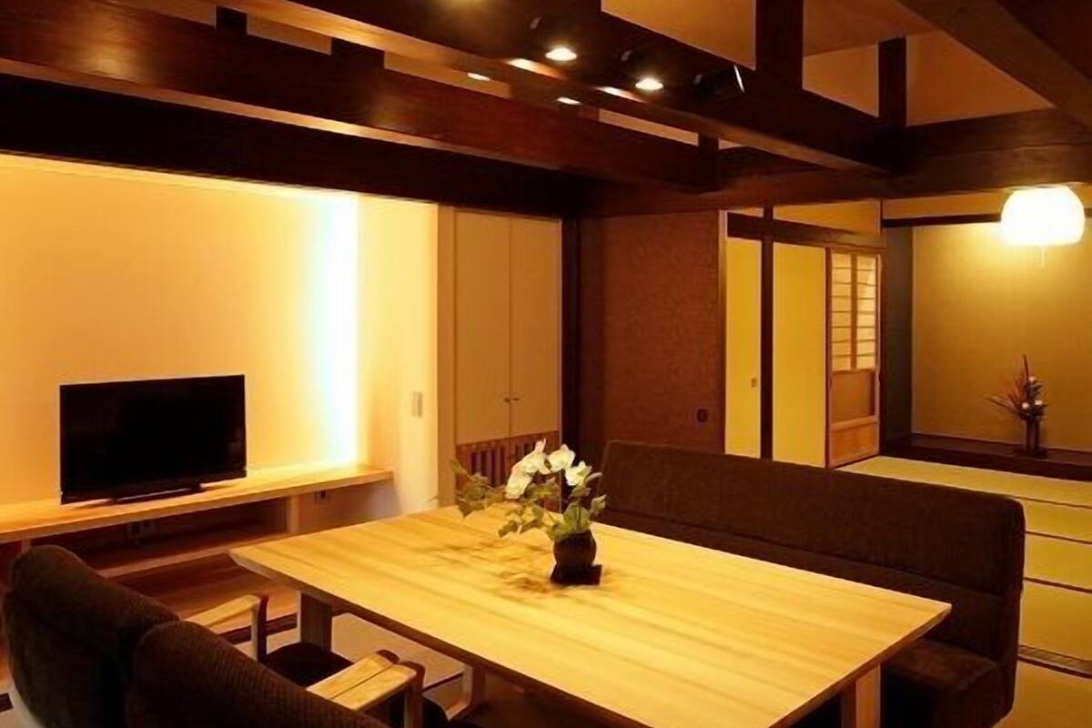 A traditional Japanese-style room with tatami flooring, a low table with cushions, and a television on a stand.