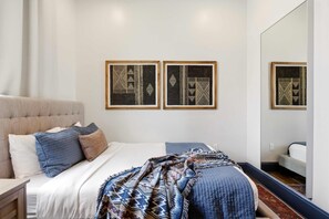 A bedroom with a bed, pillows, a blanket, and two framed wall art pieces. - 7BR City Condo | Pool Access Near CBD (New Orleans)