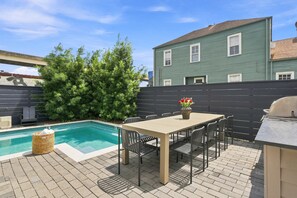 A backyard with a swimming pool, a dining table with chairs, a grill, and a large bush. - 7BR City Condo | Pool Access Near CBD (New Orleans)