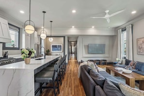 A modern kitchen with a marble countertop, bar stools, and a dining area with a sofa and coffee table. - 7BR City Condo | Pool Access Near CBD (New Orleans)
