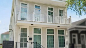 A two-story residential building with a front porch, a staircase, and a black mailbox. - 7BR City Condo | Pool Access Near CBD (New Orleans)