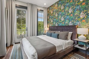A bedroom with a large bed, two bedside tables with lamps, a window with curtains, and a colorful wall mural.