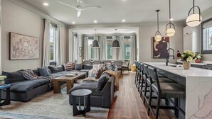 A spacious living room with a sofa set, a coffee table, and a dining area with chairs. - 7BR City Condo | Pool Access Near CBD (New Orleans)
