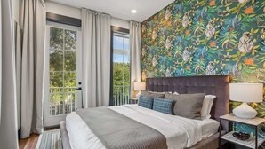 A bedroom with a large bed, two bedside tables, a window with curtains, and a colorful wall mural. - 7BR City Condo | Pool Access Near CBD (New Orleans)