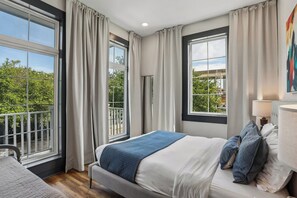 A bedroom with a bed, a bedside table, a lamp, and a view of greenery outside. - 7BR City Condo | Pool Access Near CBD (New Orleans)