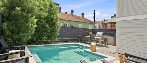 Une piscine avec un espace patio comprenant des chaises longues et un barbecue.