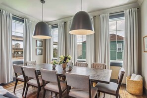 Un espace repas comprenant une grande table, des chaises, des luminaires suspendus et une vue sur l’extérieur.