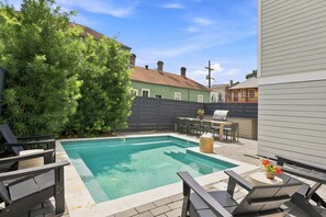 Une piscine avec un espace patio comprenant des chaises longues et un barbecue.